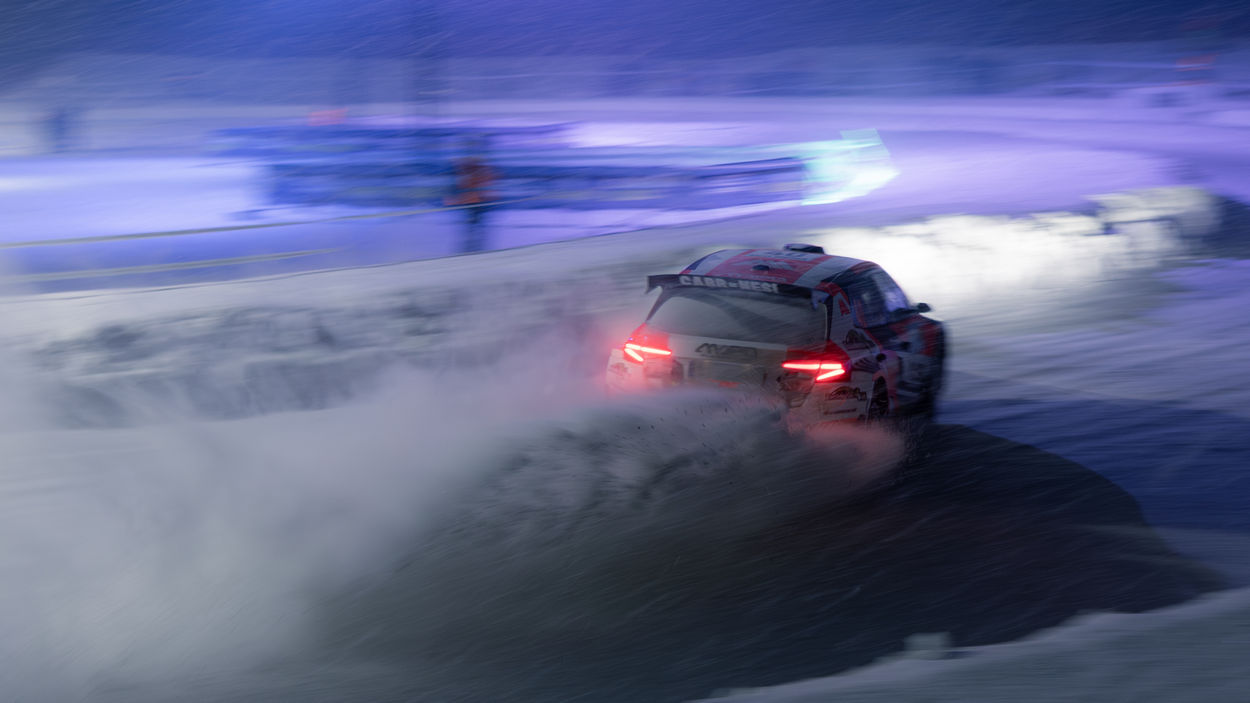 En rallybil kör i hög hastighet på en vinterväg i kvällsljus.